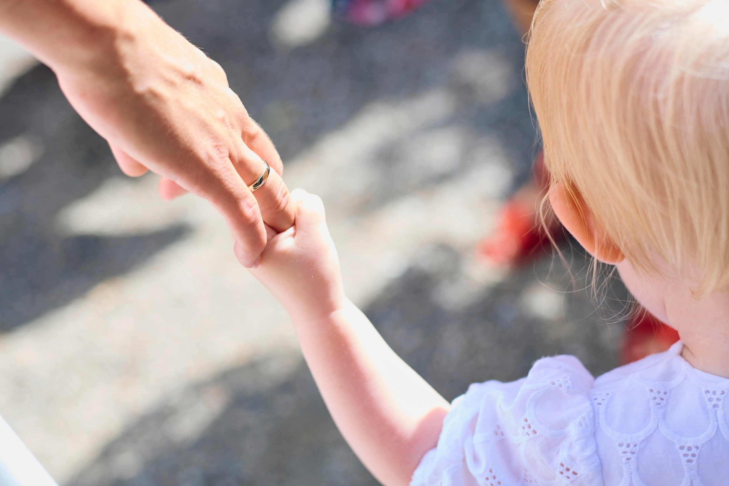 An adult holding a small child's hand as they walk outside together.
